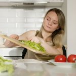 A woman preparing a fresh salad with lettuce and tomatoes in a modern kitchen.