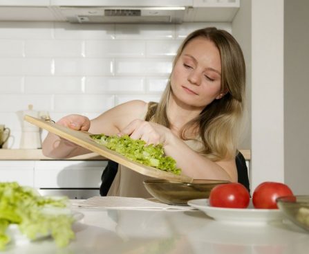 A woman preparing a fresh salad with lettuce and tomatoes in a modern kitchen.